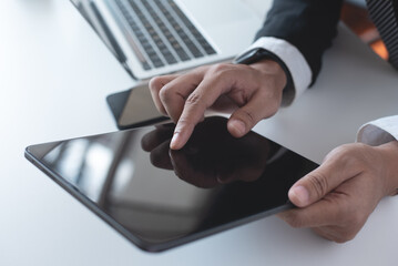 Business man in black suit using digital tablet on desk at office. Businessman finger touching on blank screen tablet, online working with laptop computer on office table, close up