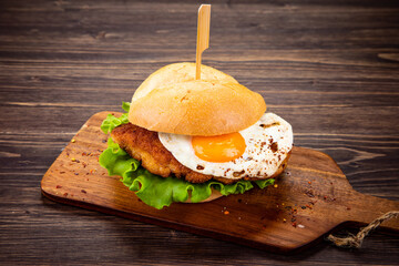Tasty schnitzel sandwich with sunny side up egg served on cutting board
