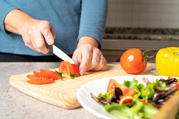 Woman cutting tomatoes on a wooden board in the kitchen at home to prepare salad. Healthy and delicious food concept. High quality photo