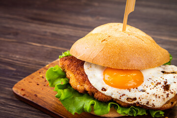 Tasty schnitzel sandwich with sunny side up egg served on cutting board
