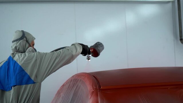 mechanic worker painting car part at automobile repair service station with spraing paint