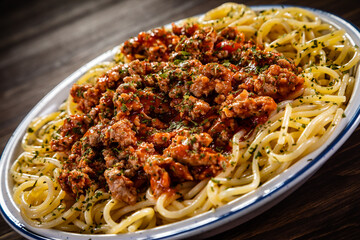 Spaghetti with minced meat, tomato sauce, parmesan cheese and seasonings served on wooden table
