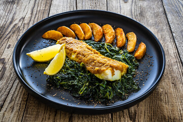 Fish dish - roast cod fillet with potatoes and spinach served on stone plate on wooden table
