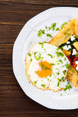 Savory crepes with feta, fried vegetables and egg on wooden background