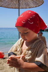 A kid in a red bandana on the seashore. Summer sea holidays. Family summer vacation. Happy little boy at the beach.