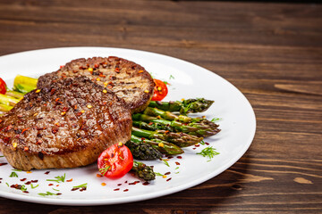 Barbecued beef steak with green asparagus on wooden table
