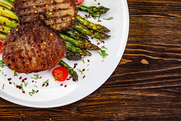 Barbecued beef steak with green asparagus on wooden table
