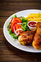 Barbecue chicken drumsticks with French fries, lettuce, tomatoes and ketchup on wooden table
