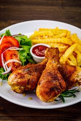 Barbecue chicken drumsticks with French fries, lettuce, tomatoes and ketchup on wooden table
