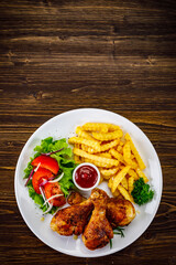 Barbecue chicken drumsticks with French fries, lettuce, tomatoes and ketchup on wooden table
