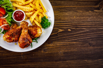 Barbecue chicken drumsticks with French fries, lettuce, tomatoes and ketchup on wooden table
