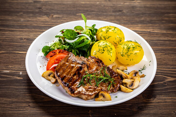 Fried beef steak with boiled potatoes and vegetables on wooden table
