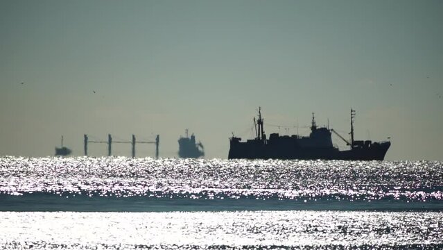 Mirage of cargo ship in the sea beyond the horizon. Fishing ship sailing in the sea. Small waves on the golden surface of warm water with bokeh lights from the sun. Sea, nature and outdoor travel.