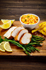 Sliced tasty roast chicken breast, green asparagus and cabbage on wooden table 