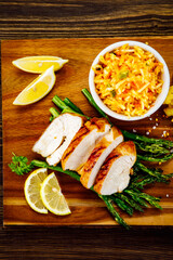 Sliced tasty roast chicken breast, green asparagus and cabbage on wooden table 