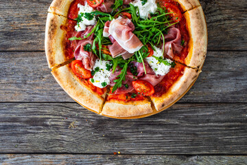 Pizza parma - prosciutto di parma, arugula, mozzarella, tomatoes, burrata on wooden table
