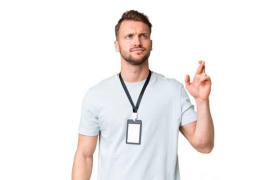 Young caucasian man with ID card over isolated chroma key background with fingers crossing and wishing the best