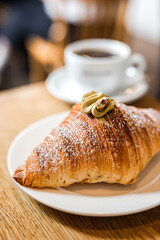 A delicious pistachio croissant and a cup of black coffee at the wooden table of a coffee shop