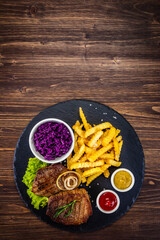 Fried beef sirloin with potatoes and vegetables on black stone plate on wooden table
