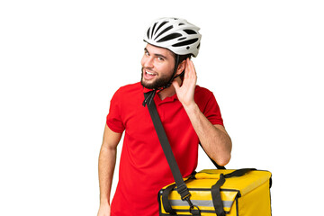 Young delivery man with thermal backpack over isolated chroma key background listening to something by putting hand on the ear