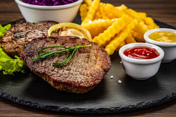 Fried beef sirloin with potatoes and vegetables on black stone plate on wooden table
