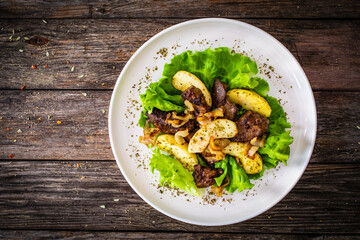 Fried liver with apples and onion on wooden table
