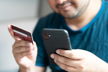 A happy man is using a credit cards and mobile phones for online payment. Shopping online at home