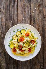 Tagliatelle with parmesan, zucchini, tomato and cream sauce on wooden table

