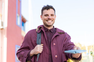 Young caucasian man at outdoors holding a passport with happy expression