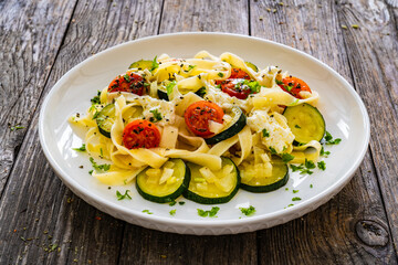 Tagliatelle with parmesan, zucchini, tomato and cream sauce on wooden table
