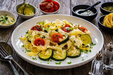 Tagliatelle with parmesan, zucchini, tomato and cream sauce on wooden table
