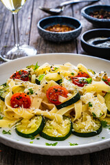 Tagliatelle with parmesan, zucchini, tomato and cream sauce on wooden table
