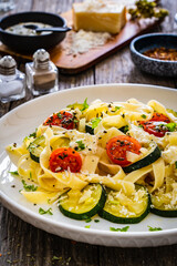 Tagliatelle with parmesan, zucchini, tomato and cream sauce on wooden table
