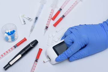 Glukometr medyczny trzymany w dłoni obok strzykawek - obrazy, fototapety, plakaty