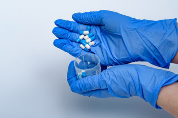 Leki trzymane w dłoni w niebieskich rękawiczkach wsypywane do pojemnika - obrazy, fototapety, plakaty