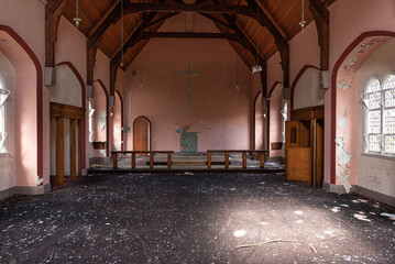 Derelict church interior, vandalised, with broken lights, peeling paint on  walls and glass strewn floor.