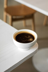 A white cup of black coffee americano on the edge of a table in a cafe