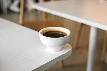 A white cup of black coffee americano on the edge of a table in a cafe