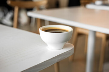 A white cup of black coffee americano on the edge of a table in a cafe