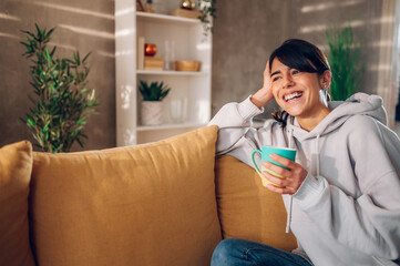 Beautiful woman using smartphone and drinking coffee on the sofa at home