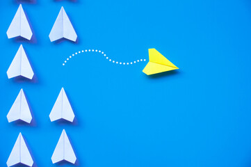 Yellow paper airplane origami leaving other white airplanes on blue background with customizable space for text or ideas. Leadership skills concept and copy space