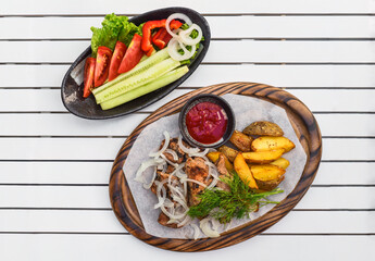 Pork shashlik with grilled vegetables served with salad and ketchup on wooden board
