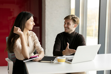Beautiful brunette girl talking with handsome man sitting at desk. Concept of work in modern office