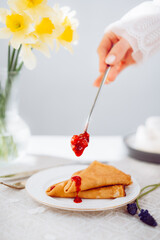 A woman in a white dress is holding a spoonful of strawberry jam on a plate with a plate of pancakes