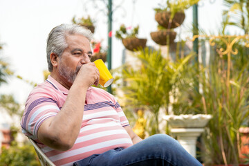 Happy senior man drinking a cup of coffee or tea in his garden.