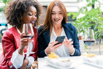 Two women sharing a funny moment as they watch videos on their phone. Smiling and enjoying each other's company, they sitting outdoors at garden.