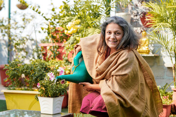 Indian Senior woman watering the flowers in the garden.