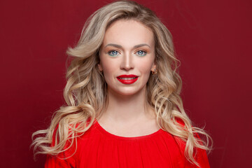 Fototapeta premium Nice woman with long curly blonde hair against red studio wall background