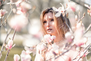Fototapeta premium Portrait of a beautiful happy middle aged woman enjoying the smell in a blooming spring garden. Beautiful magnolia bushes, large flowers.