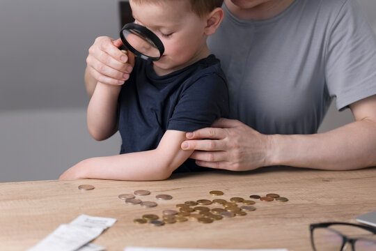 A little boy looks at coins through a magnifying glass. A child with his mother sorts through the coins on the table and counts the money. Business concept. Child and money. High quality photo